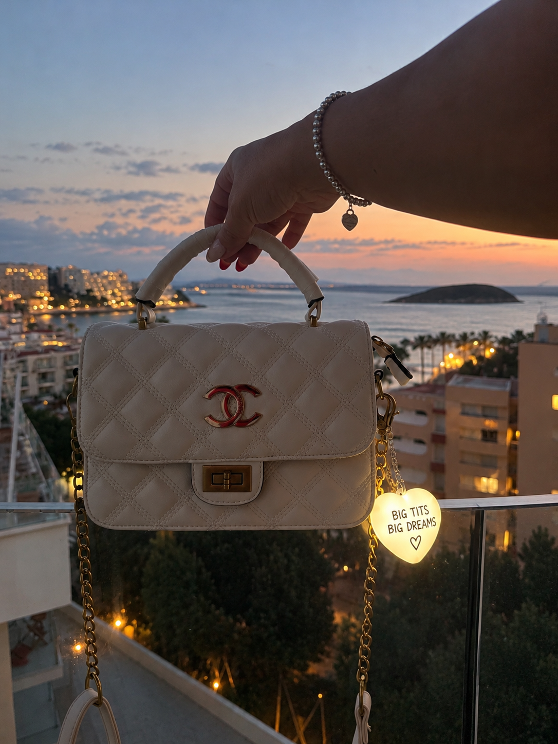 Bitchology light-up handbag charm on a white quilted bag at sunset, showing Big Tits Big Dreams design